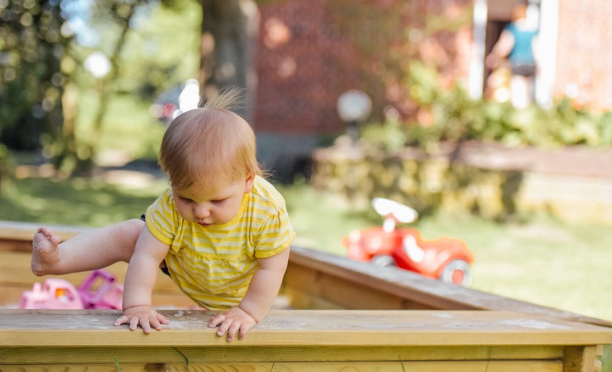 Toddler climbing out of sandpit wearing reusable nappies and incontinence aids from an NDIS plan
